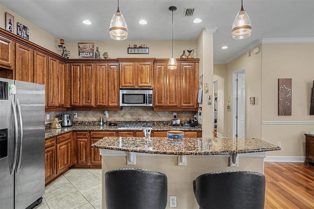 A kitchen features wood cabinets, granite countertops, stainless steel appliances, and a breakfast bar — 3614 WIREGRASS ROAD, NEW PORT RICHEY, FL