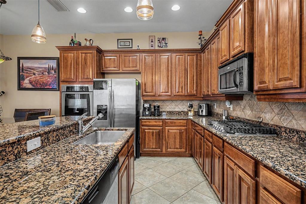 A kitchen features wood cabinets, granite countertops, stainless steel appliances, and a tile floor — 3614 WIREGRASS ROAD, NEW PORT RICHEY, FL