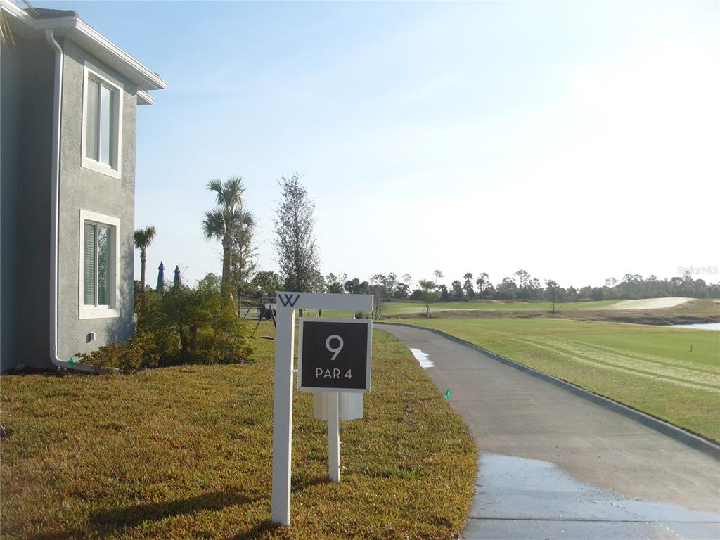 A golf course hole sign stands near a paved path next to a residential building — 17540 OPAL SAND DRIVE UNIT 204, VENICE, FL