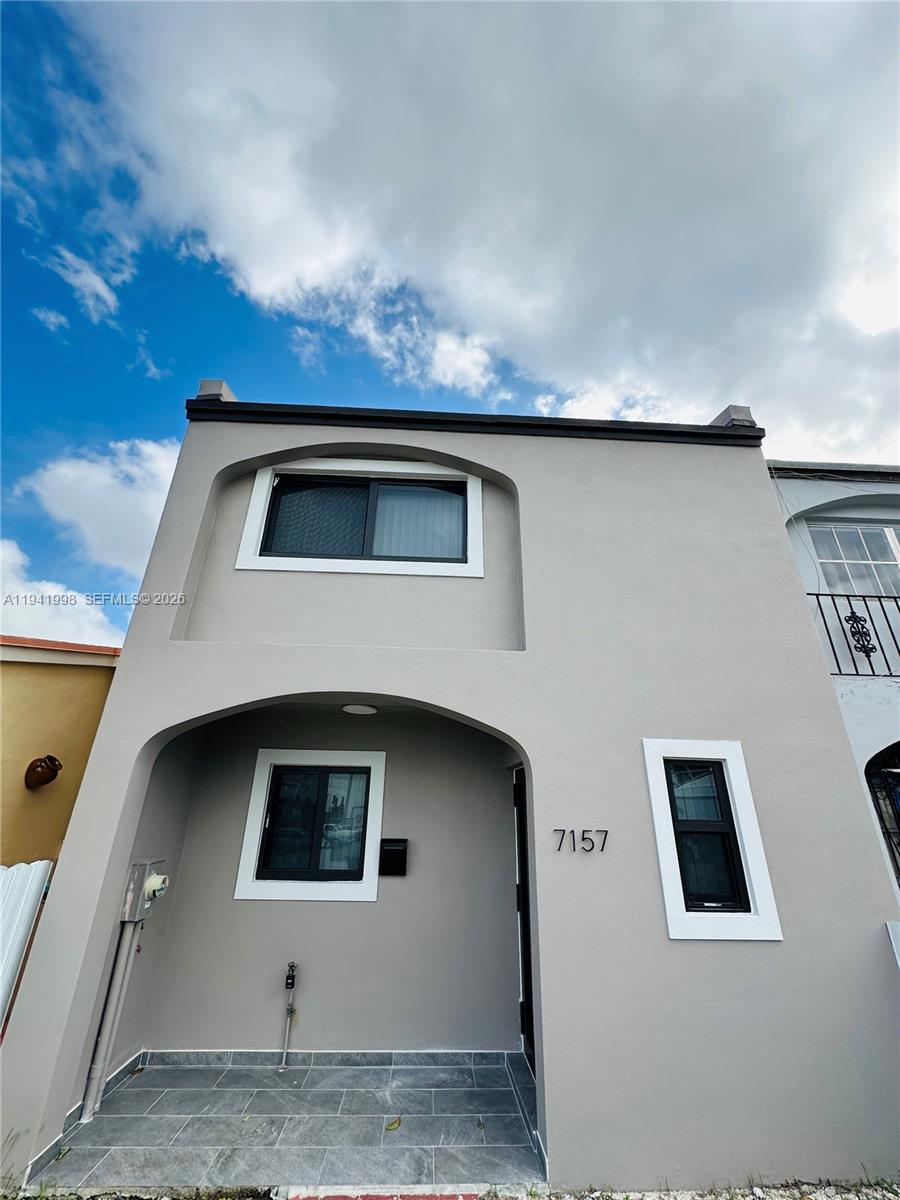 A two-story gray stucco townhouse features a tiled entryway and black-framed windows — 7157 W 19th Ct # 7157, Hialeah FL 33014, HIALEAH, FL