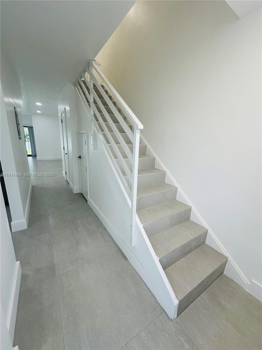 A staircase with white railings and gray tiled steps sits in a minimalist hallway — 7157 W 19th Ct # 7157, Hialeah FL 33014, HIALEAH, FL