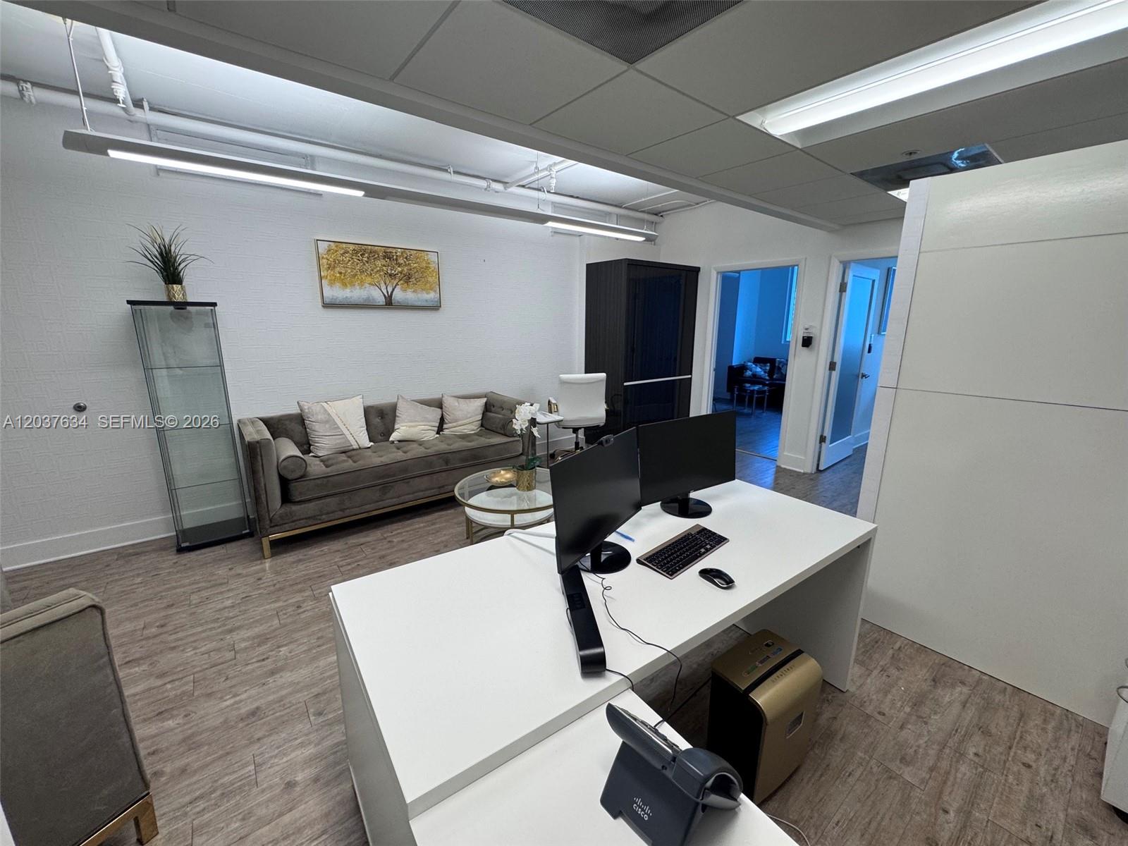 An office space features a white desk, a grey sofa, and a glass display cabinet — 40 SW 13th St # 402, Miami FL 33130, MIAMI, FL