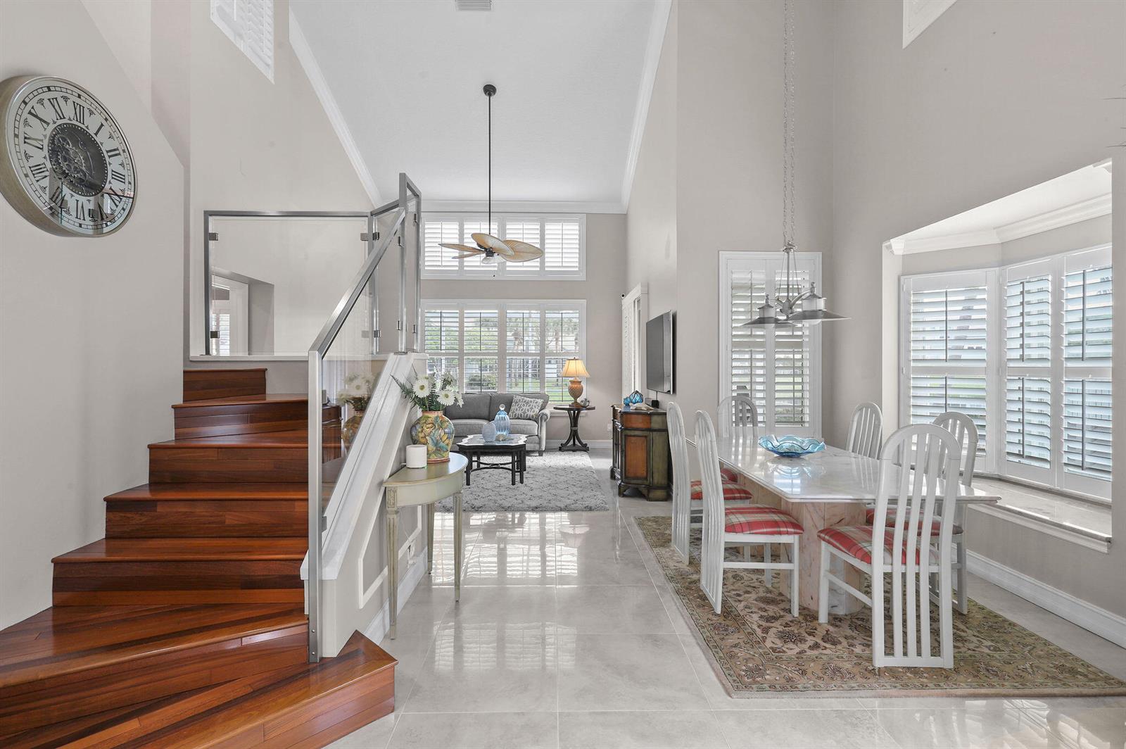 A bright, open-concept dining and living area features a wooden staircase, tile floors, and shutters — 2056 Windward Way, Jupiter FL 33477, JUPITER, FL