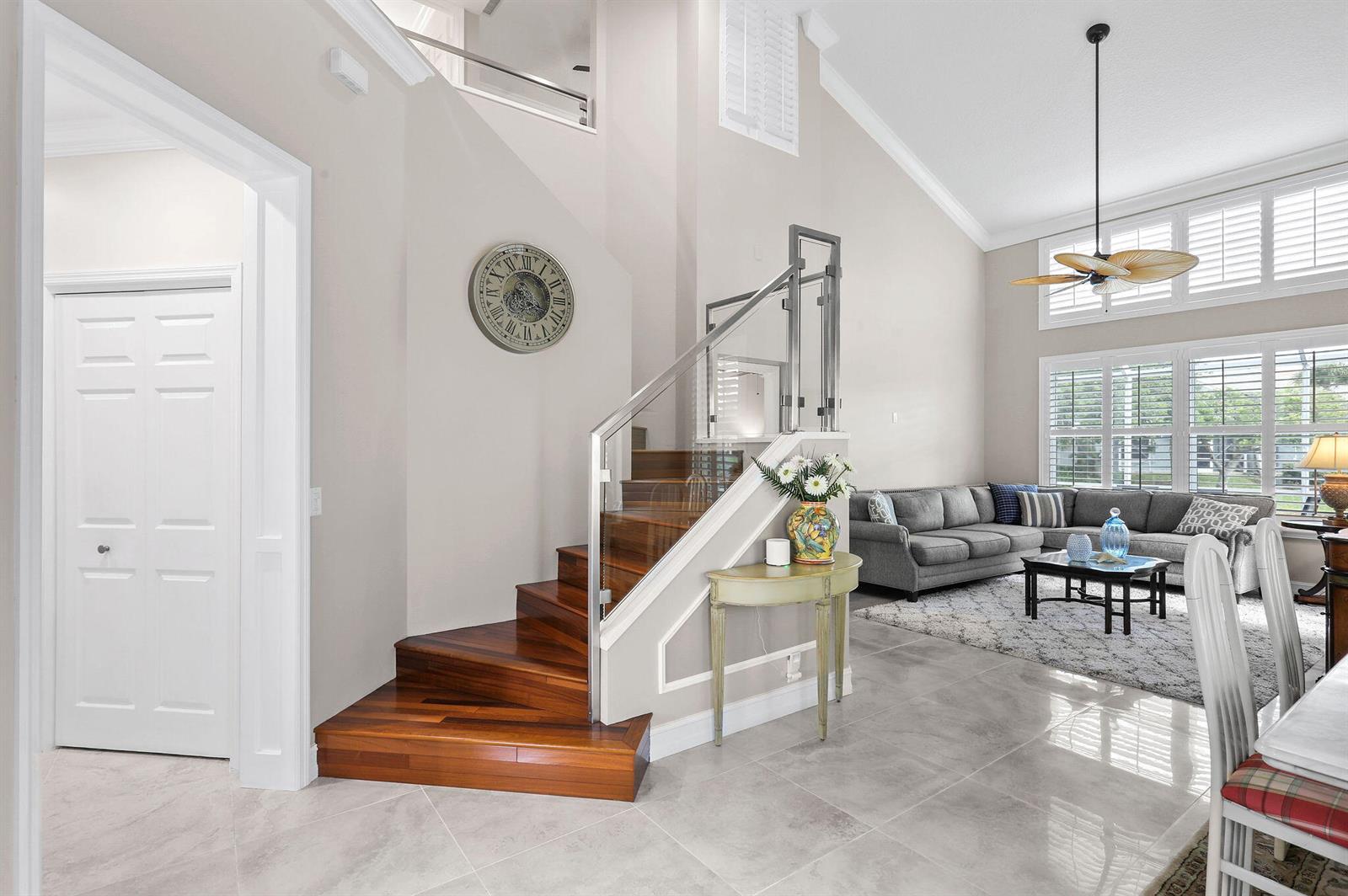 A living room with a wooden staircase, glass railing, tile floors, and a gray sofa — 2056 Windward Way, Jupiter FL 33477, JUPITER, FL