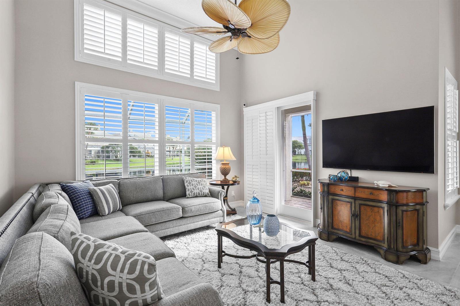 A living room features a grey sectional sofa, a glass coffee table, and plantation shutters — 2056 Windward Way, Jupiter FL 33477, JUPITER, FL