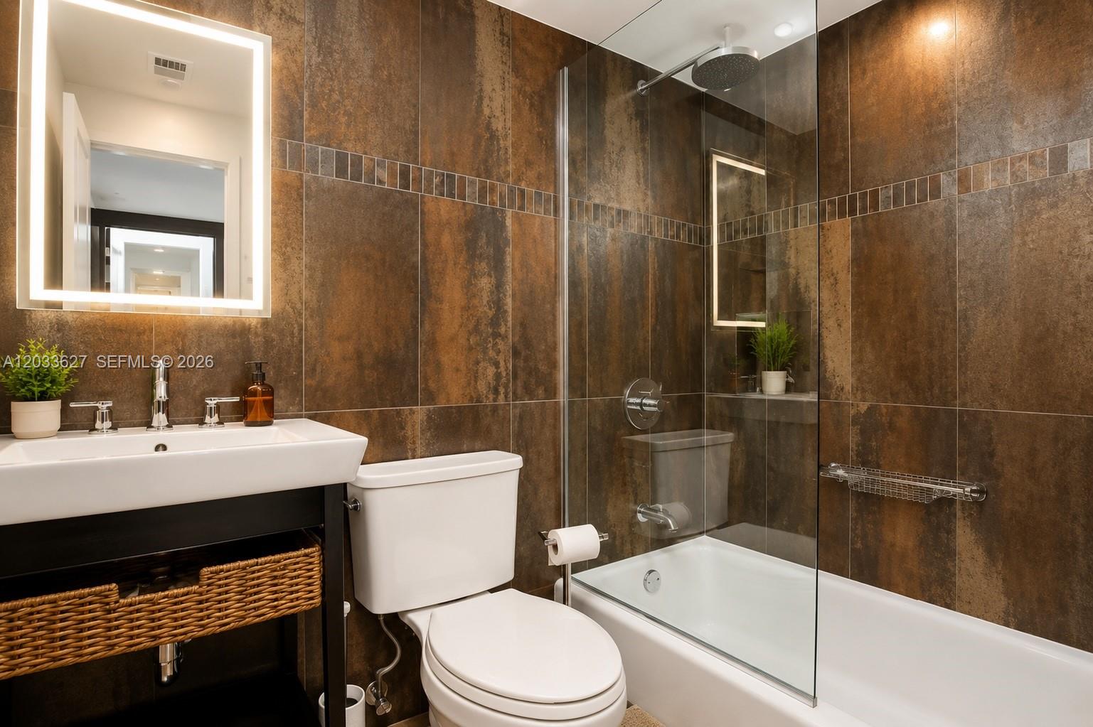 A bathroom features dark brown tiled walls, a white vanity, and a glass-enclosed bathtub — MIAMI BEACH, FL