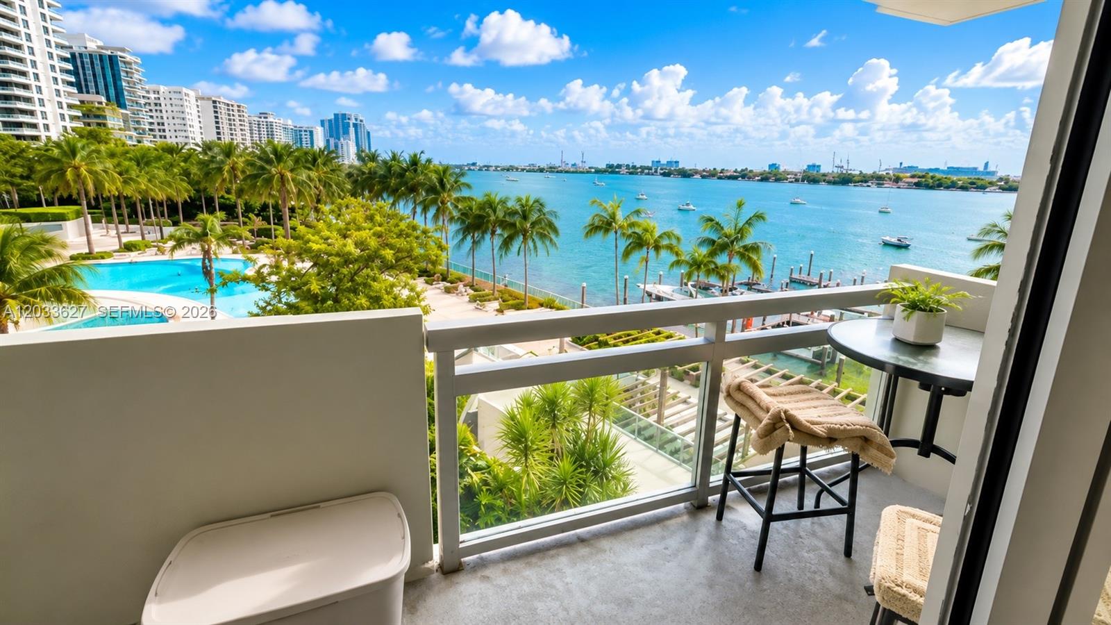A balcony overlooks a swimming pool, palm trees, and a bay with boats — MIAMI BEACH, FL