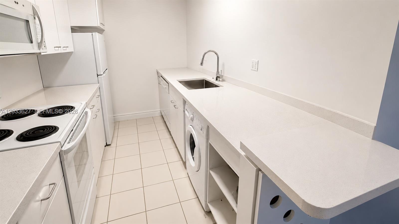 A galley-style kitchen features white cabinets, a refrigerator, a stove, and a built-in washer — MIAMI BEACH, FL