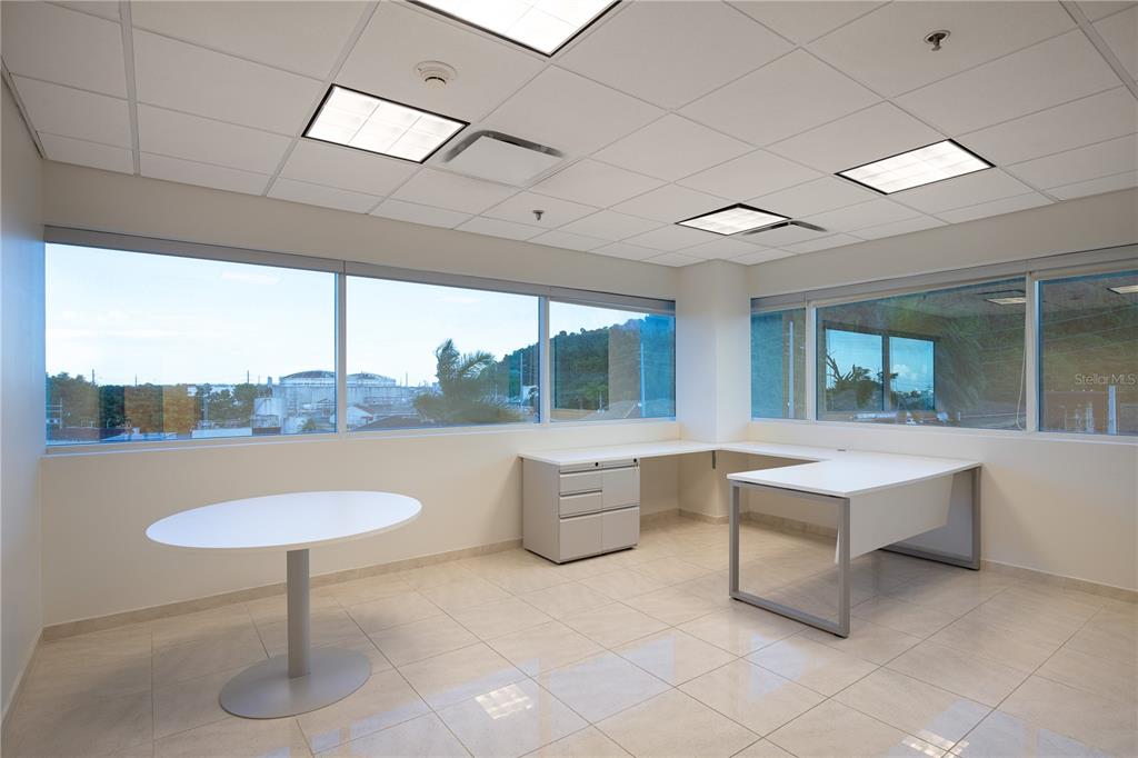 An office space features a white desk, a round table, tile floors, and large windows — 90 CARR 165 SUITE 309 CENTRO INTERNACIONAL DE MERCADEO, GUAYNABO, PR