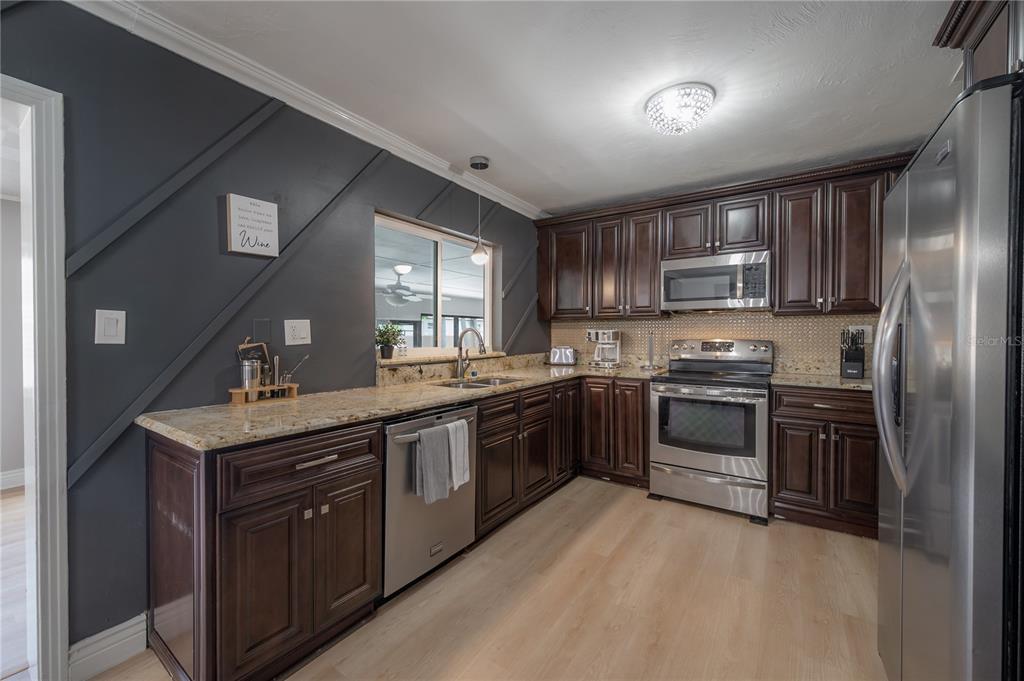 A kitchen features dark wood cabinets, granite countertops, stainless steel appliances, and a dark accent wall — 2916 W COLLINS STREET, TAMPA, FL
