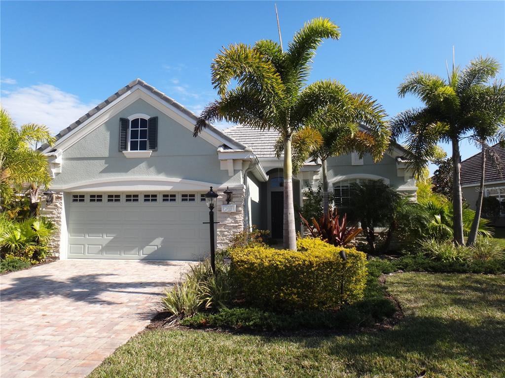 A single-story house with a light green exterior, stone accents, a two-car garage, and palm trees — 12051 THORNHILL COURT, LAKEWOOD RANCH, FL