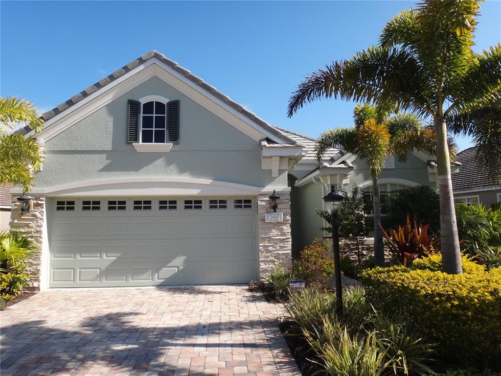 A light green house with a stone facade, a two-car garage, and palm trees — 12051 THORNHILL COURT, LAKEWOOD RANCH, FL