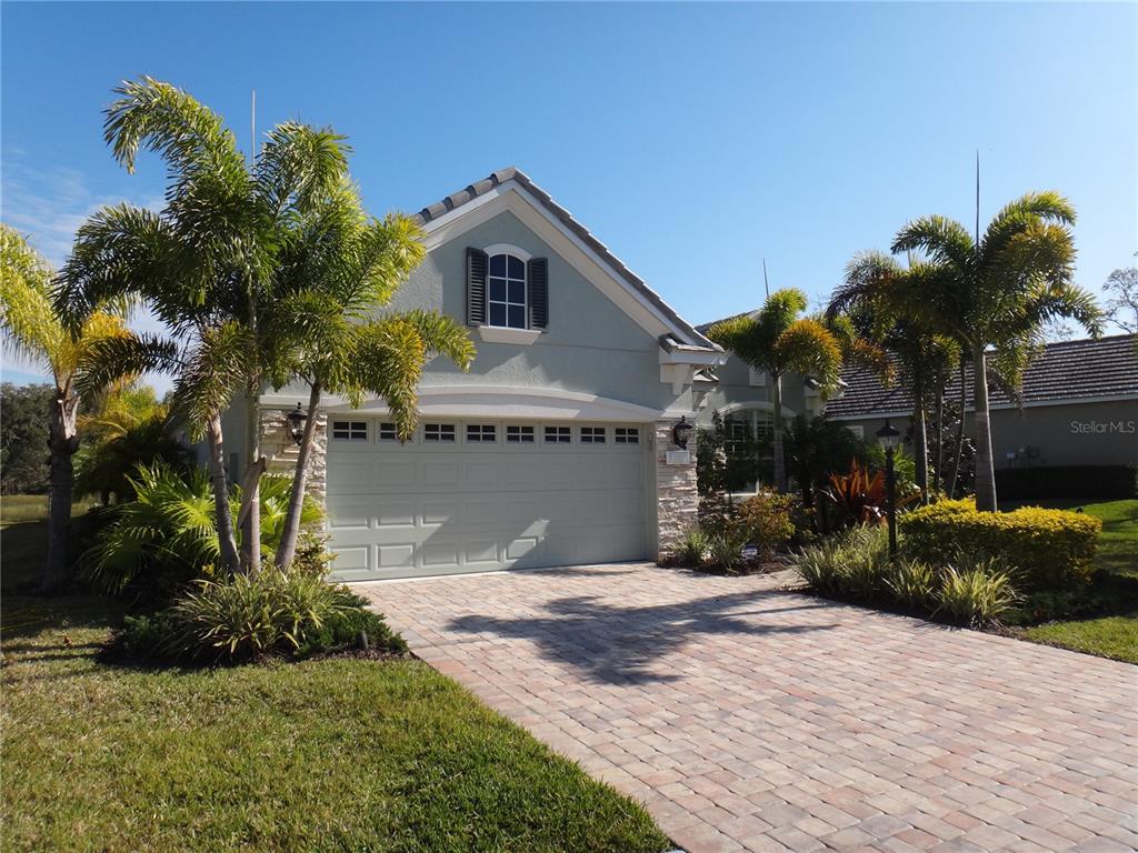 A light green house with a stone-accented garage and a paver driveway under palm trees — 12051 THORNHILL COURT, LAKEWOOD RANCH, FL