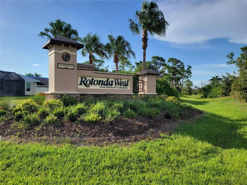 A tan monument sign for Rotonda West stands in a landscaped grassy area with palm trees — 95 LONG MEADOW LANE, ROTONDA WEST, FL