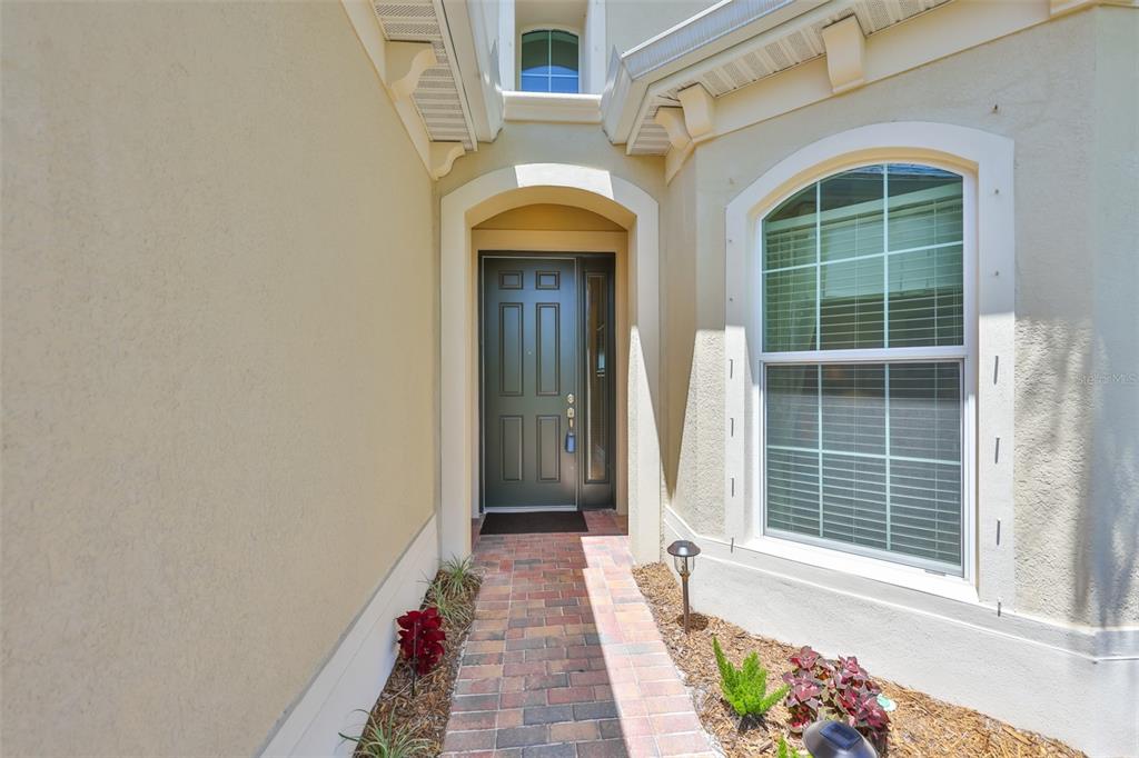 A brick walkway leads to a dark front door with a side window and arched entryway — 1809 PACIFIC DUNES DRIVE, SUN CITY CENTER, FL