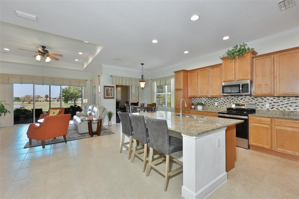 An open-concept kitchen with granite countertops and wood cabinets overlooks a living area and patio — 1809 PACIFIC DUNES DRIVE, SUN CITY CENTER, FL