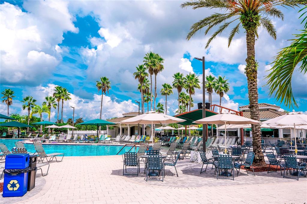 A swimming pool area with lounge chairs, umbrellas, and palm trees under a cloudy sky — 2110 S HALCYON DRIVE UNIT 456, SUN CITY CENTER, FL