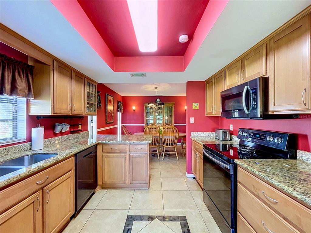 A kitchen with wood cabinets, granite countertops, and red walls opens into a dining area — 2110 S HALCYON DRIVE UNIT 456, SUN CITY CENTER, FL