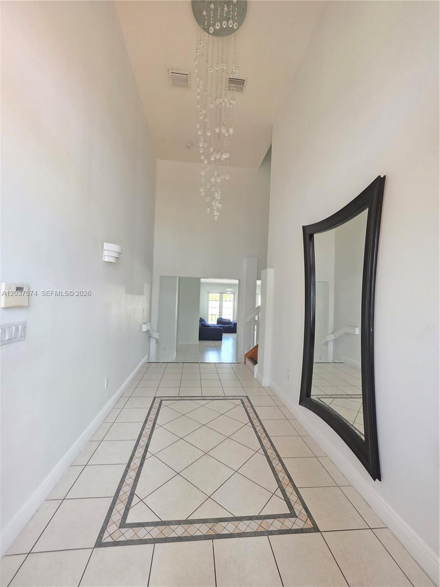 A high-ceilinged foyer features tile flooring, a crystal chandelier, and a double wooden door — 14291 SW 34th St, Miami FL 33175, MIAMI, FL
