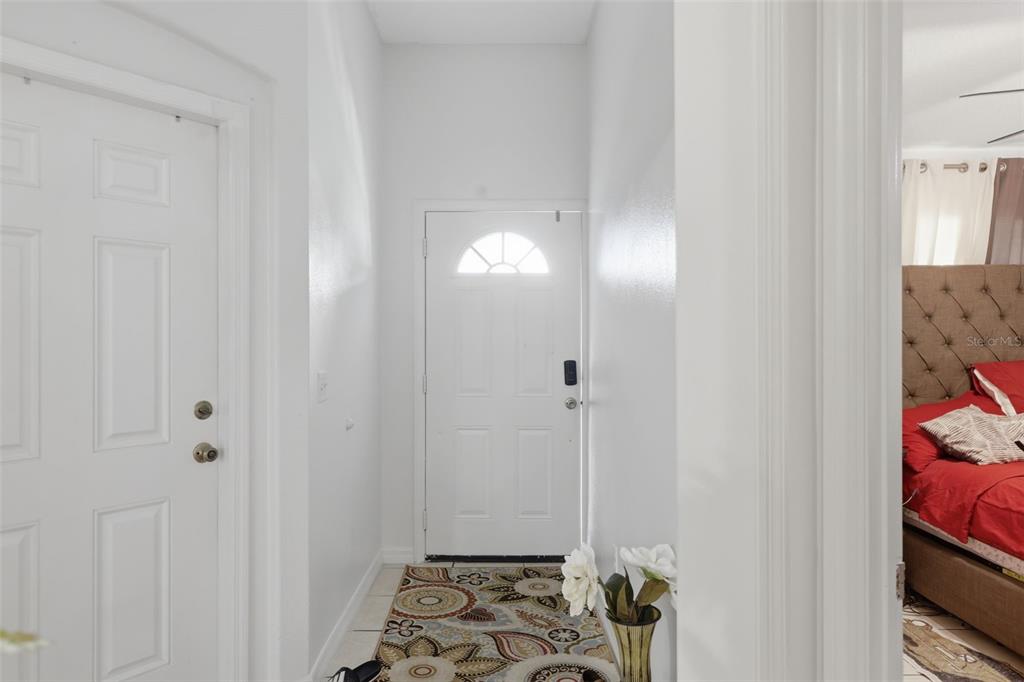 A white front door opens into a small entryway with a patterned rug and tile flooring — 1911 S GADSEN BOULEVARD, ORLANDO, FL