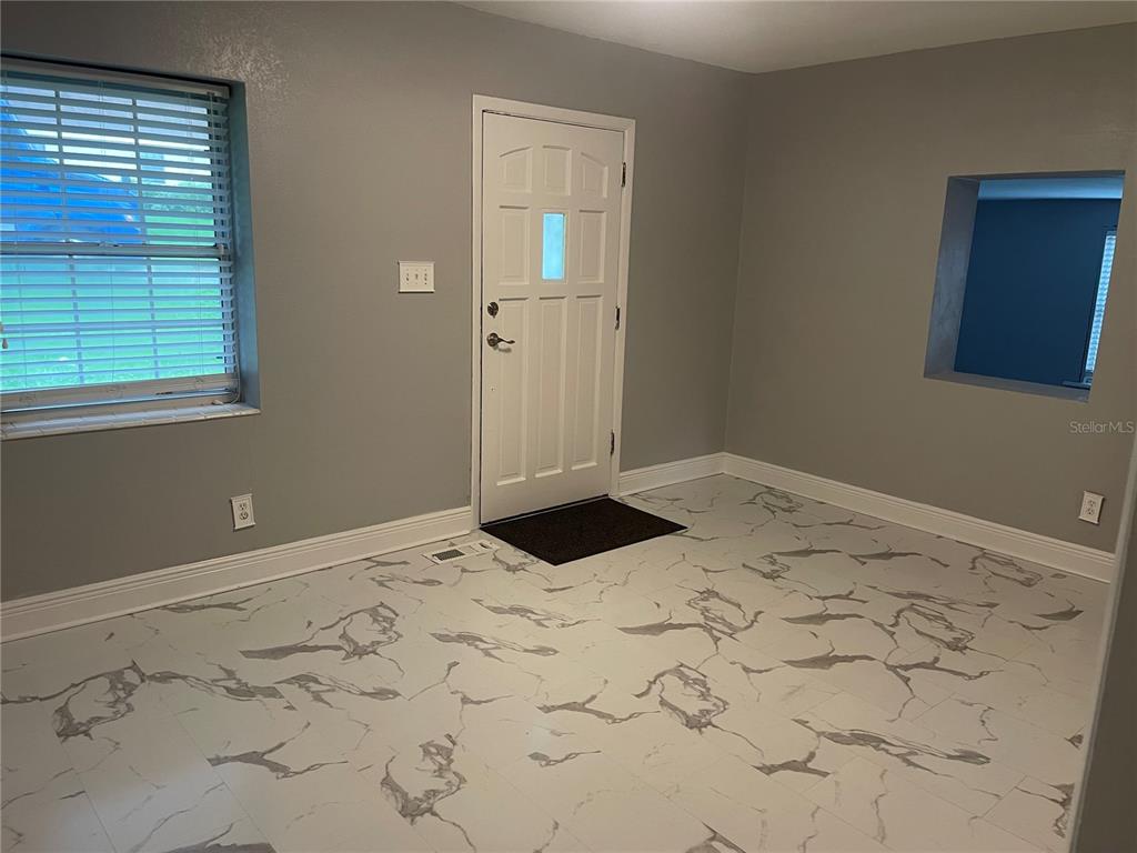 A room with gray walls, white marble-patterned tile flooring, a front door, and a window — 1108 CUERNO STREET, TALLAHASSEE, FL