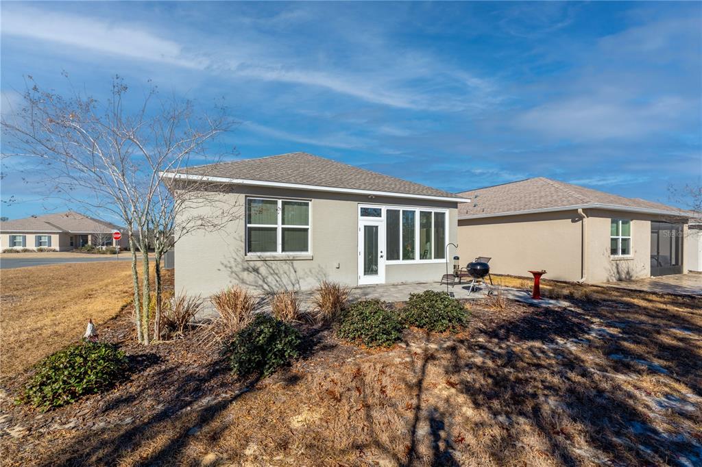 The exterior back view of a beige house features a patio, landscaping, and a grill — 9325 SW 106TH AVENUE, OCALA, FL