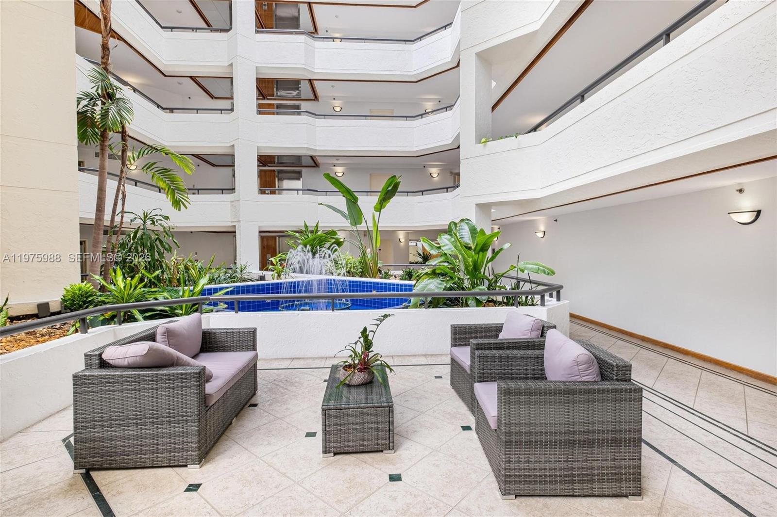 An indoor atrium features a tiered balcony design, a central fountain, and patio furniture — 170 Ocean Lane Dr # 310, Key Biscayne FL 33149, KEY BISCAYNE, FL