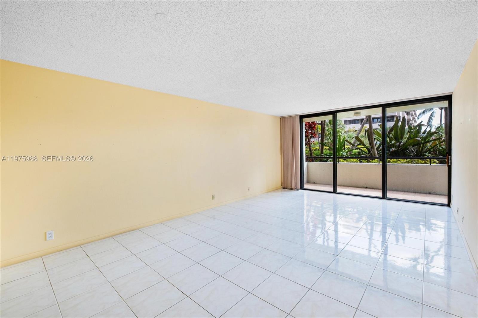 An empty living room features light yellow walls, white tile flooring, and a sliding glass door — 170 Ocean Lane Dr # 310, Key Biscayne FL 33149, KEY BISCAYNE, FL