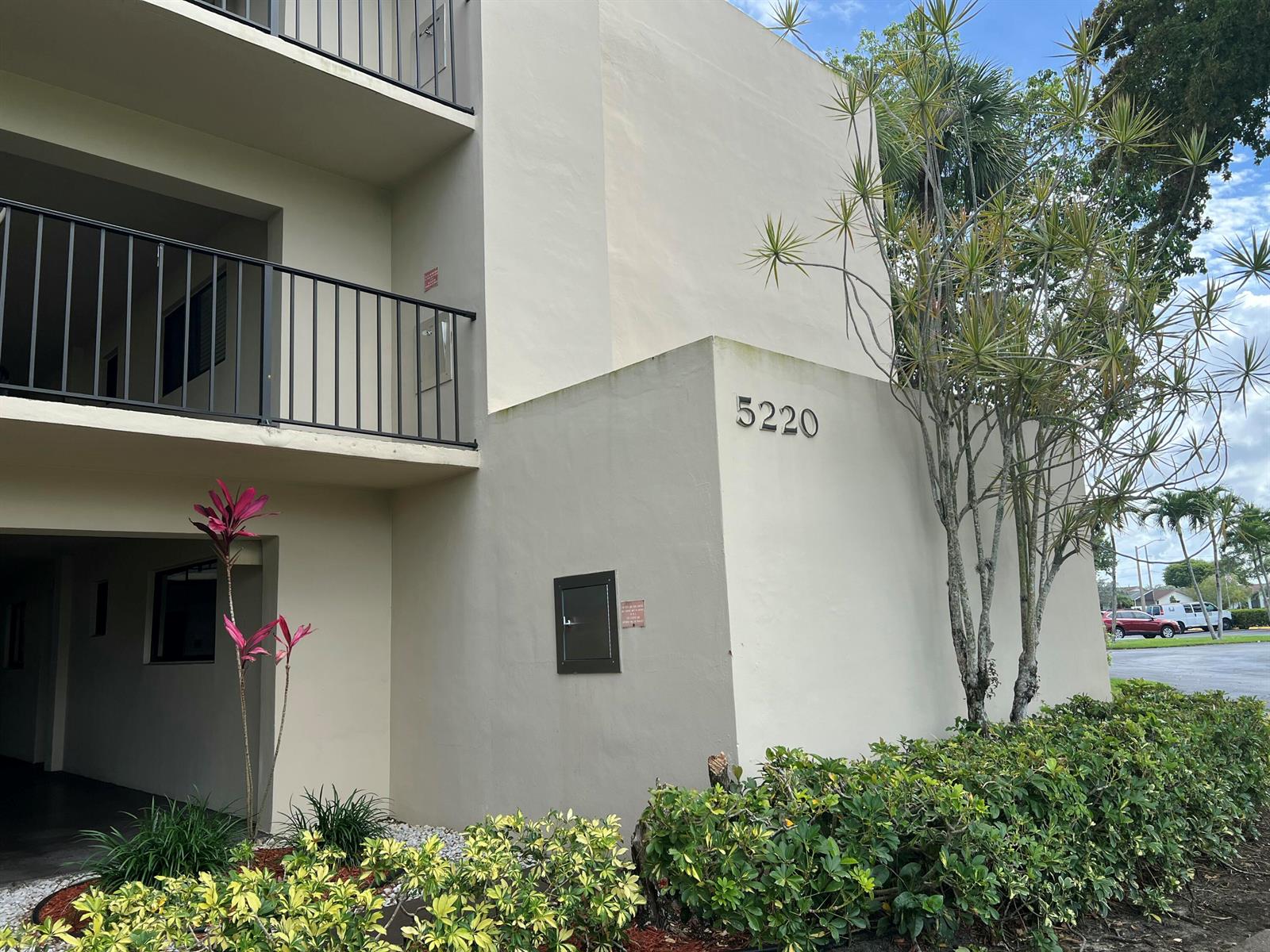 The exterior of a multi-story apartment building features a beige stucco facade and black railings — 5220 Las Verdes Circle # 101, Delray Beach FL 33484, DELRAY BEACH, FL