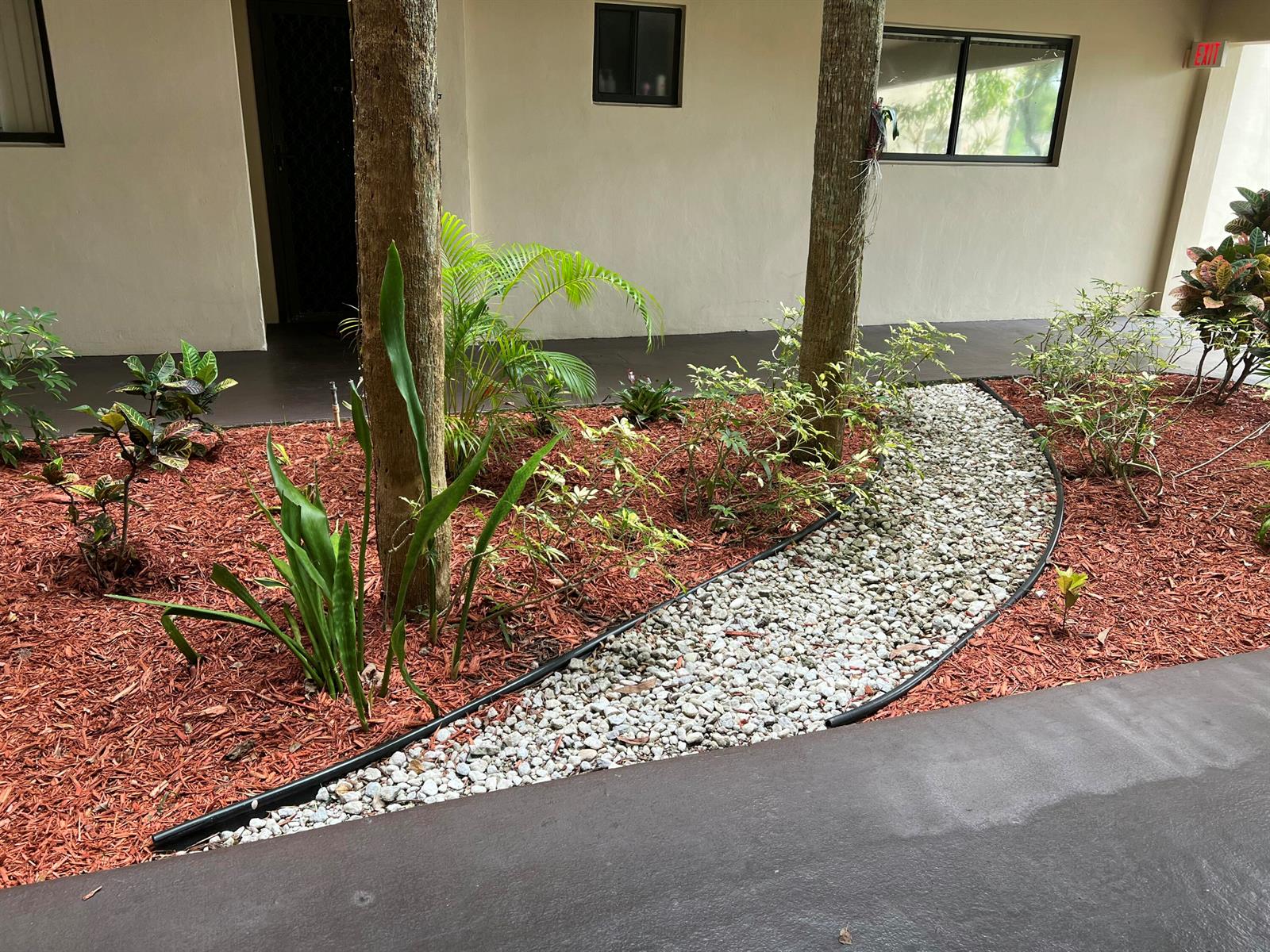 A landscaped garden bed features red mulch, white gravel, and small trees near a building — 5220 Las Verdes Circle # 101, Delray Beach FL 33484, DELRAY BEACH, FL
