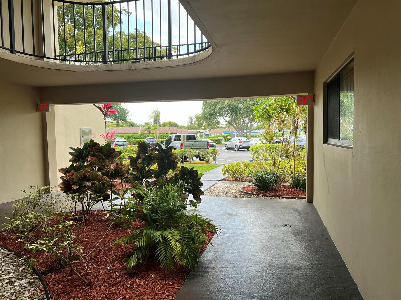A covered outdoor walkway leads to a parking lot with landscaping and a circular opening — 5220 Las Verdes Circle # 101, Delray Beach FL 33484, DELRAY BEACH, FL