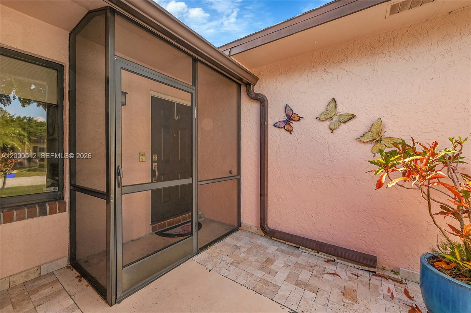 A screened-in entryway features a dark door, tiled flooring, and butterfly wall decor — 14664 Bonaire Boulevard # 1, Delray Beach FL 33446, DELRAY BEACH, FL