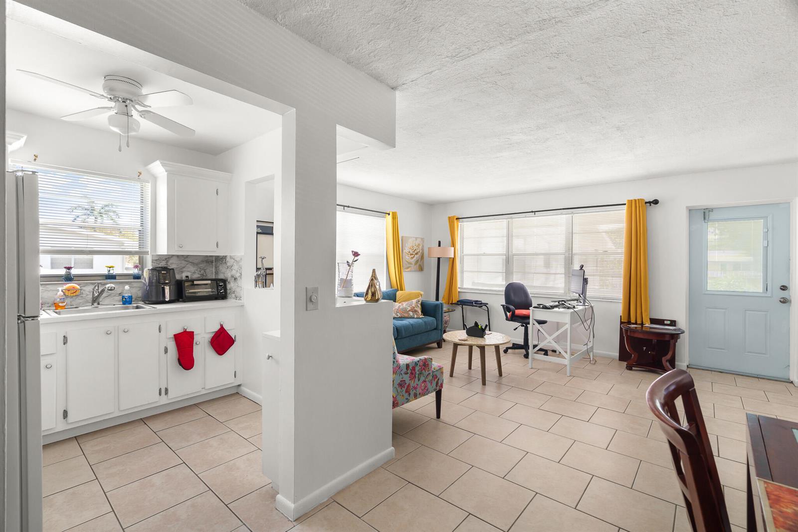A kitchen with white cabinets opens into a living area with tile floors and yellow curtains — 347 Windsor O, West Palm Beach FL 33417, WEST PALM BEACH, FL