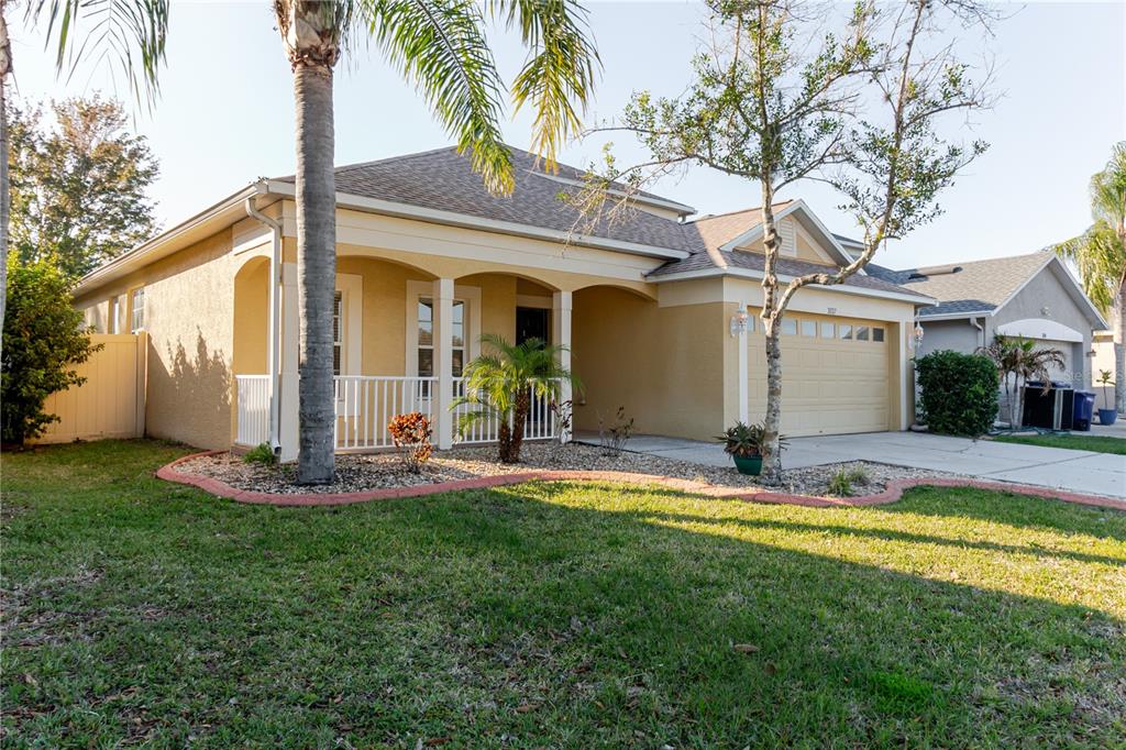 A single-story house with a tan stucco exterior, a covered front porch, and a two-car garage — 3037 DOWNAN POINT DRIVE, LAND O LAKES, FL