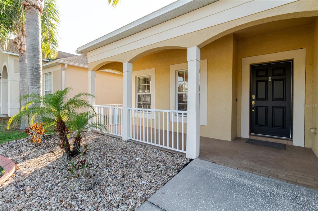 A tan house exterior features a covered porch with white railings and a black door — 3037 DOWNAN POINT DRIVE, LAND O LAKES, FL