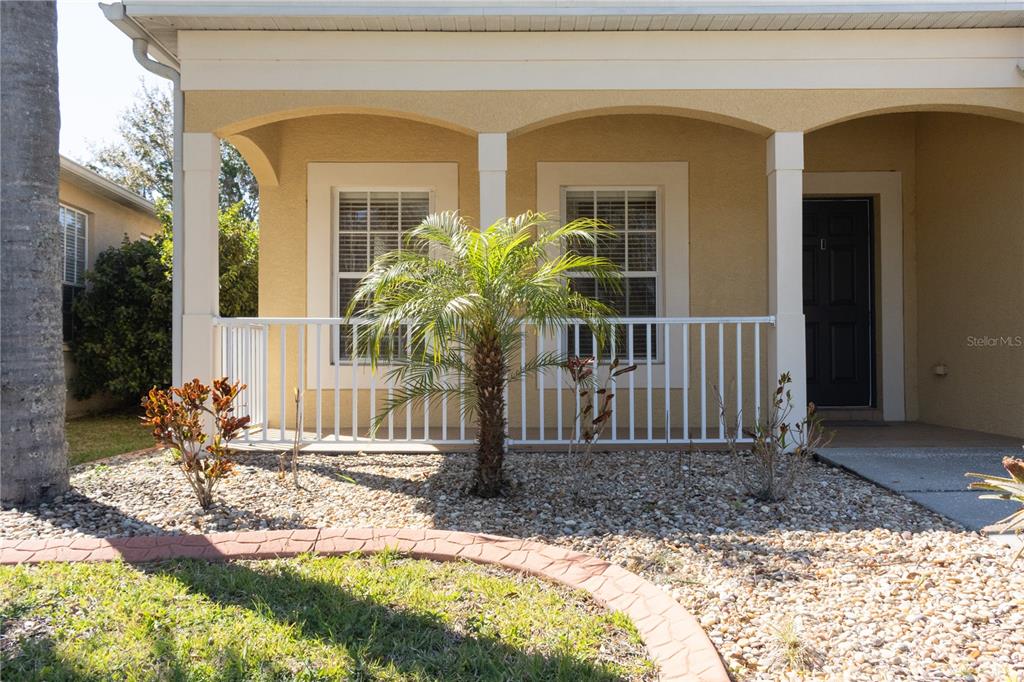 A tan house exterior features a front porch with a white railing and a palm tree — 3037 DOWNAN POINT DRIVE, LAND O LAKES, FL