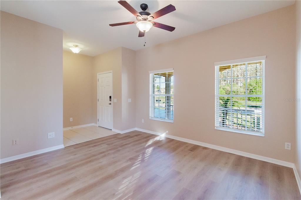 An empty living room with light wood-look flooring, beige walls, and a ceiling fan — 3037 DOWNAN POINT DRIVE, LAND O LAKES, FL