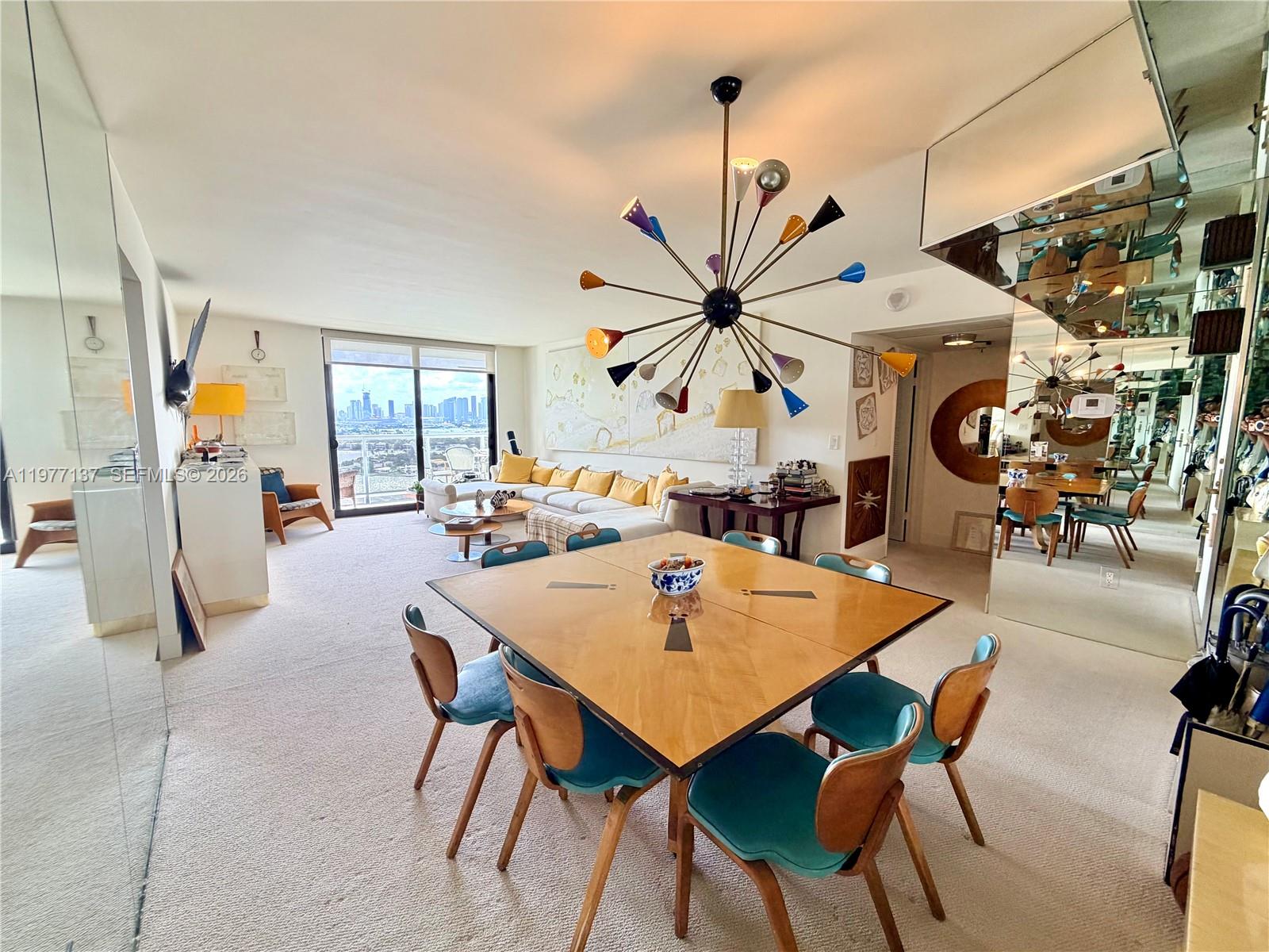 A dining area with a square wooden table and teal chairs sits before a living room — 9 Island Ave # 2304, Miami Beach FL 33139, MIAMI BEACH, FL