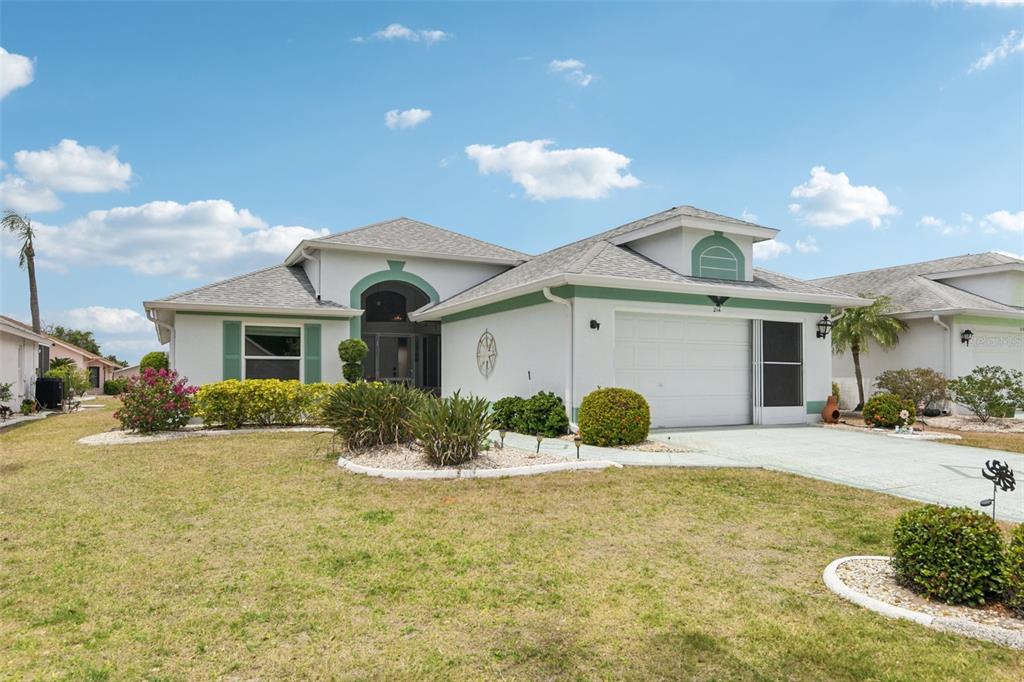 A single-story house with a white stucco exterior, green trim, and a two-car garage — 214 LINGER LANE, SUN CITY CENTER, FL