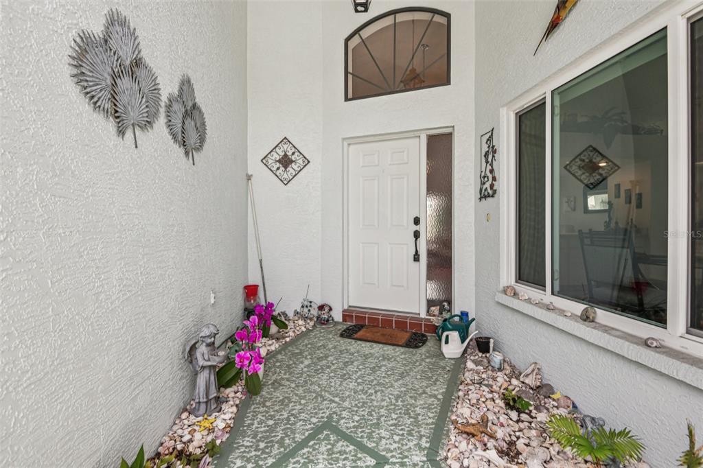 A covered entryway features a white front door, a decorative arched window, and shell-covered landscaping — 214 LINGER LANE, SUN CITY CENTER, FL