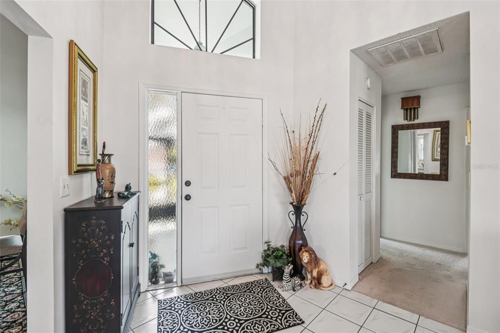 A bright entryway features a white front door, tiled floors, and a tall decorative vase — 214 LINGER LANE, SUN CITY CENTER, FL