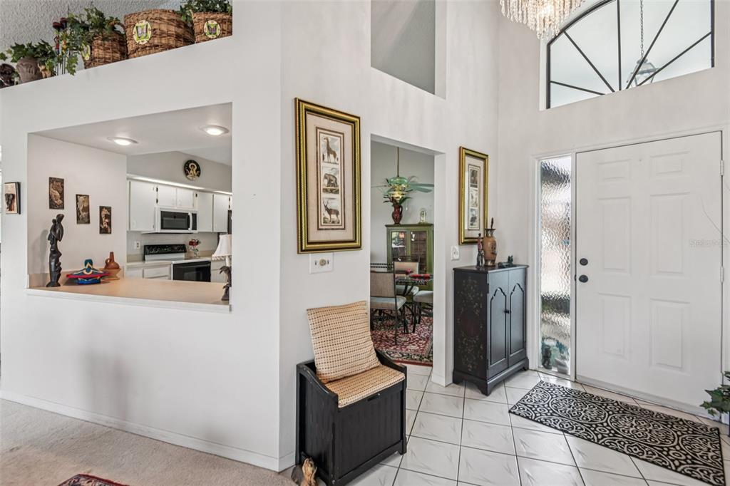 An entryway with white tile floors, a front door with a sidelight, and an open kitchen — 214 LINGER LANE, SUN CITY CENTER, FL