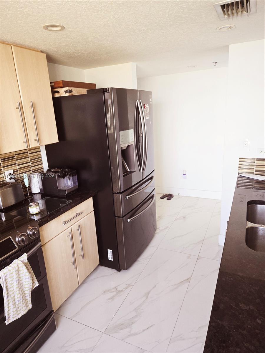 A kitchen features light wood cabinets, dark countertops, a stainless steel refrigerator, and white flooring — 1650 Coral Way # 702, Miami FL 33145, MIAMI, FL