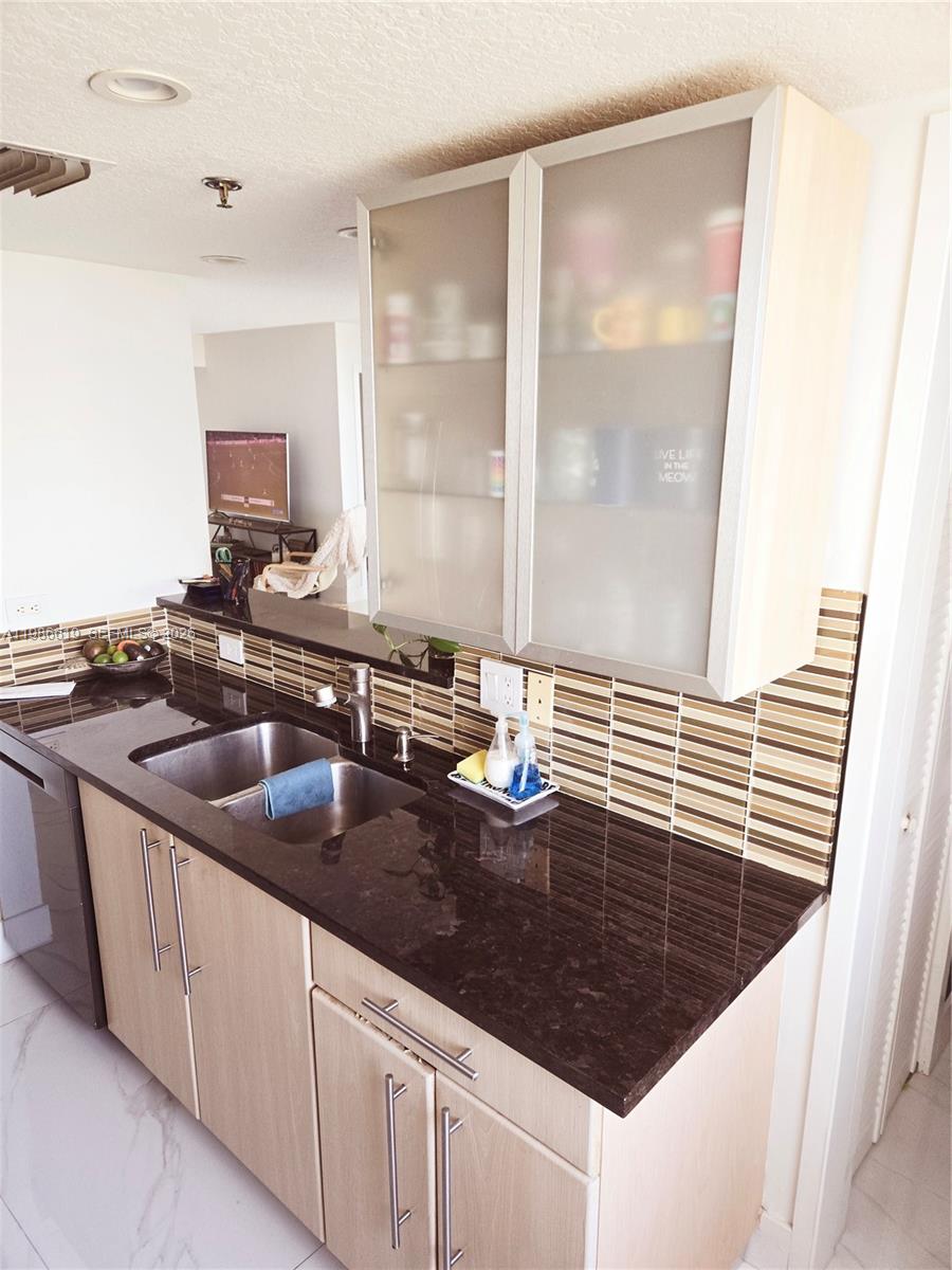A kitchen features light wood cabinets, dark granite countertops, and a brown tiled backsplash — 1650 Coral Way # 702, Miami FL 33145, MIAMI, FL