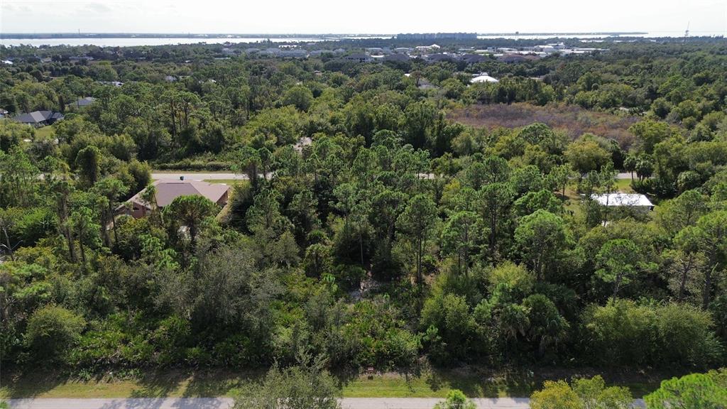 An aerial view shows a wooded, undeveloped residential lot surrounded by trees and nearby houses — 23431 RACINE AVENUE, PUNTA GORDA, FL