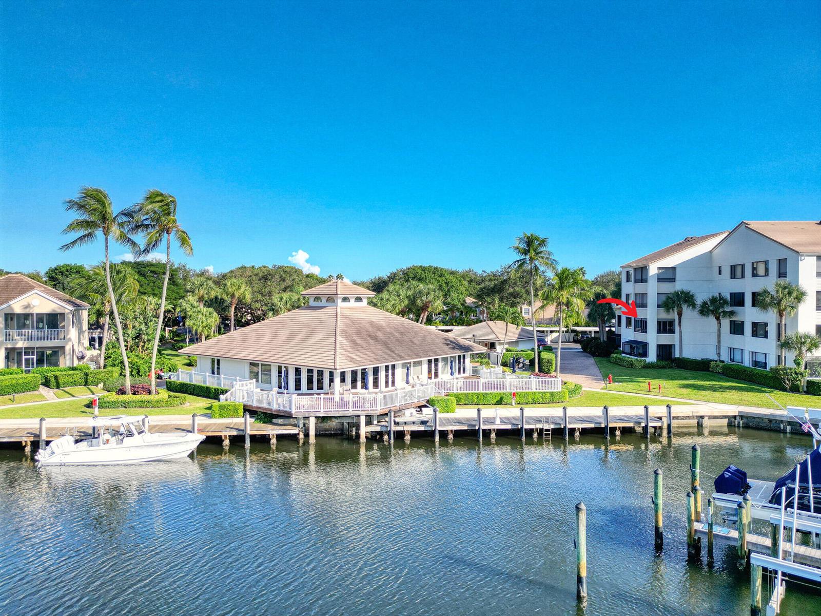An aerial view shows a waterfront clubhouse, a boat docked at a pier, and residential buildings — 827 Oak Harbour Drive, Juno Beach FL 33408, JUNO BEACH, FL