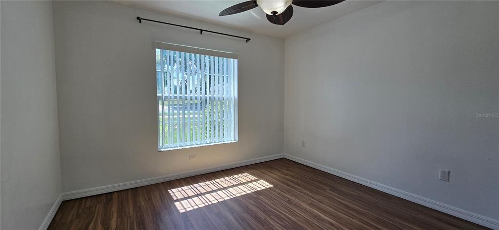 An empty bedroom features white walls, wood-look flooring, a ceiling fan, and a window with blinds — 1500 KAYUNI DRIVE, MASCOTTE, FL
