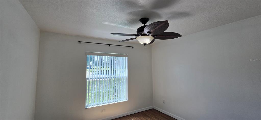 An empty room features white walls, wood-look flooring, a ceiling fan, and a window with blinds — 1500 KAYUNI DRIVE, MASCOTTE, FL
