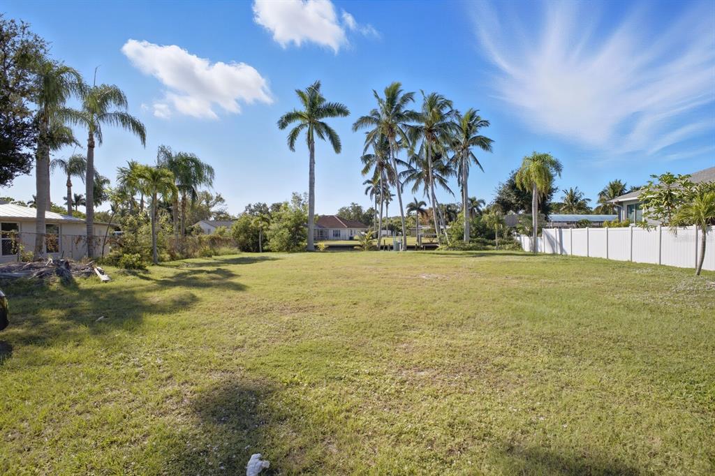 A grassy vacant lot features several palm trees and a white fence under a sky — 6915 9TH AVENUE NW, BRADENTON, FL