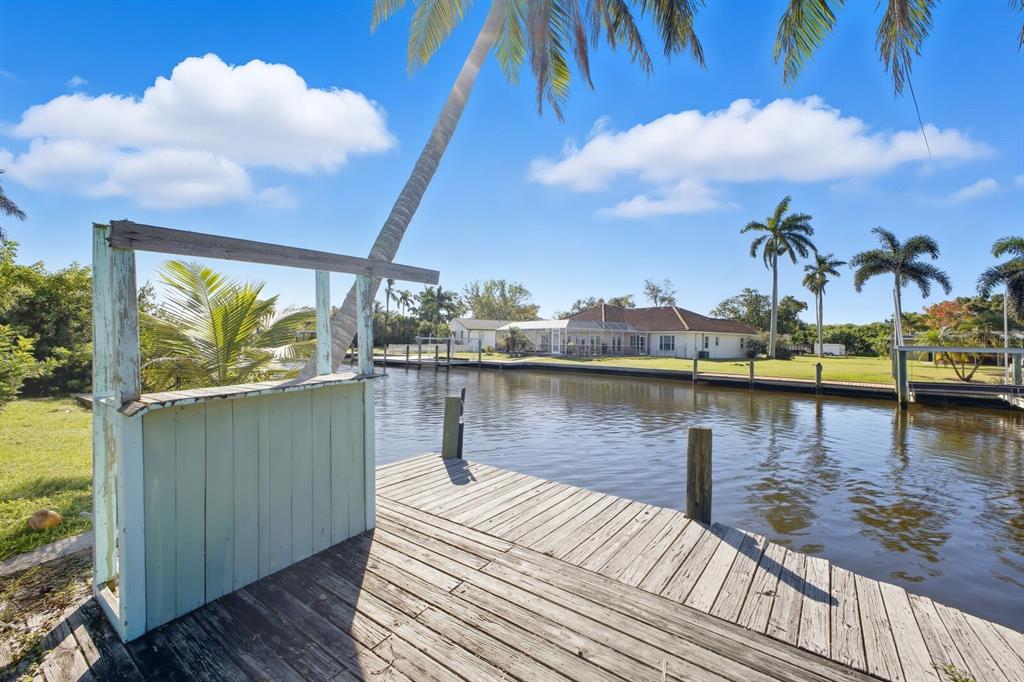 A wooden dock with a small bar structure overlooks a canal and a residential house — 6915 9TH AVENUE NW, BRADENTON, FL